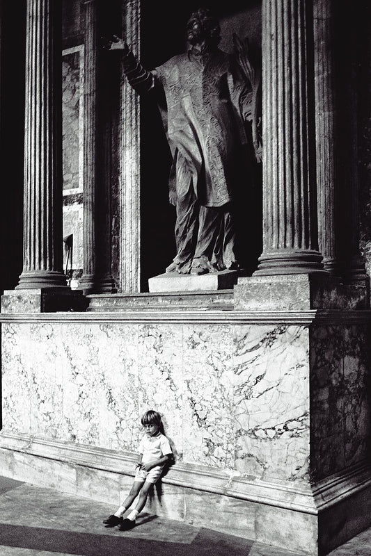 Vintage street black and white film photography, boy leaning against statue in the Pantheon, Rome. c1970